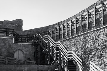 black and white shot of a medieval fortress wall with a complex structure of modern wooden stairs....