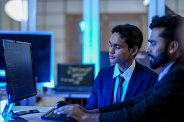 A diverse team of AI developers collaborates on a night coding session. A senior engineer oversees his team, intensely focused on debugging a complex machine learning project.