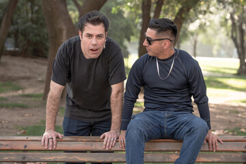Two men in a park, one looking surprised, the other wearing sunglasses.