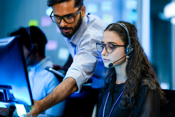 A diverse team of technical support specialists works a late shift in a busy call center. Focused operators with headsets assist clients, providing all day customer service.