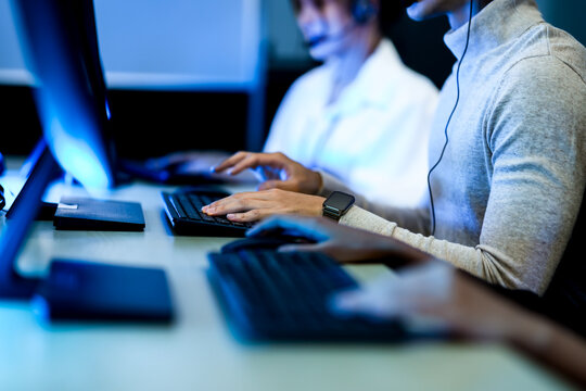 Close up of a customer service agent's hands typing on a backlit keyboard. A concept for data entry, online communication, and technical support in a modern call center office. - Powered by Adobe