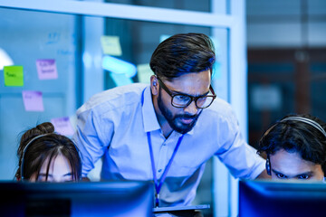 A diverse and inclusive team of software developers collaborates on a project. A female team lead discusses code with her colleagues, one of whom is in a wheelchair, in a modern office.