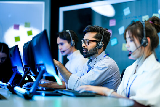 Professional call center agents with headsets providing friendly customer support. A dedicated male operator and his team work in modern all day technical assistance center.
