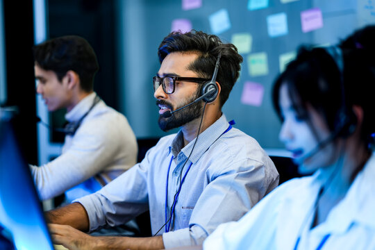 Professional call center agents with headsets providing friendly customer support. A dedicated male operator and his team work in modern all day technical assistance center.