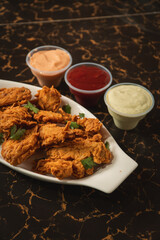 Fried chicken on a plate with sauces around it on a graphite table.