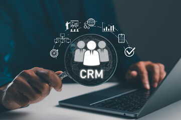 Naklejka premium A person is using a laptop with a magnifying glass focusing on a CRM (Customer Relationship Management) graphic, symbolizing data analysis and business strategy.