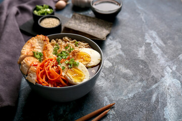 Bowl of ramen noodle soup with chicken and korean carrot salad on blue background, closeup