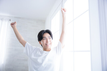 A man stretching his arms by the window in the morning, waking up refreshed. Good morning~