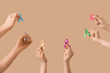 Many hands with different ribbons on beige background. Cancer awareness concept