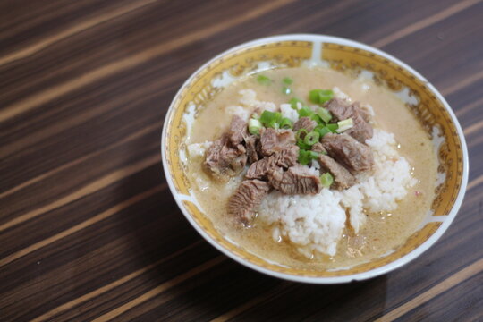 A close-up of a (coto makassar) delicious beef rice bowl with tender slices of beef, topped with fresh green onions, served in a flavorful broth.