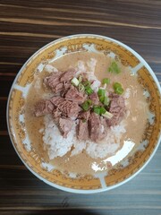 A close-up of a (coto makassar) delicious beef rice bowl with tender slices of beef, topped with fresh green onions, served in a flavorful broth.