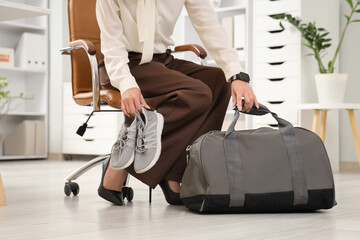 Young businesswoman with sports bag and sneakers sitting in office