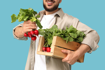 Young man with box of ripe radish on blue background, closeup