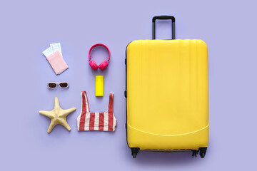 Suitcase, swimsuit and accessories on lilac background