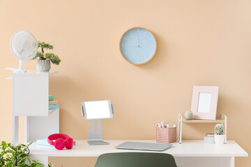 Workplace with electric fan and clock on beige wall in office