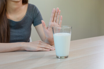 Asian woman refusing glass of milk by raising her hand, representing lactose intolerance, dairy allergy and decision to avoid milk for health or dietary reasons. Causes stomach pain and diarrhea.