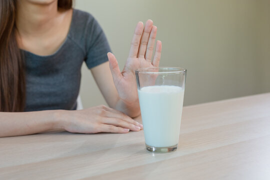 Asian woman refusing glass of milk by raising her hand, representing lactose intolerance, dairy allergy and decision to avoid milk for health or dietary reasons. Causes stomach pain and diarrhea. - Powered by Adobe