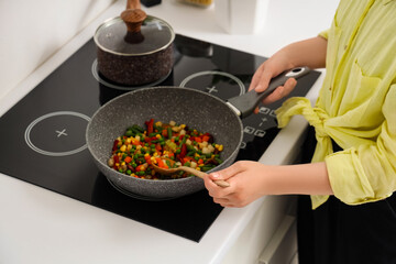 Woman with spoon frying vegetables on stove in kitchen, closeup