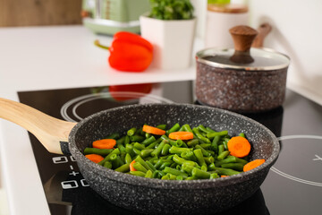Frying pan with tasty vegetables on stove in kitchen, closeup