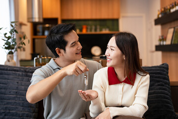 Happy young family couple holding key to new home on moving day concept, first time real estate owners man husband embrace woman wife look at camera proud buying property sitting in own flat .