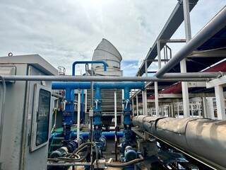 a large cooling tower and a complex network of blue and insulated industrial pipes on a rooftop. The scene highlights HVAC and mechanical systems set against a cloudy sky, suggesting a factory or comm