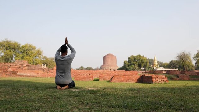 young Buddhist devotee performing holy mediation at sarnath dhamek stupa ruins under daylight