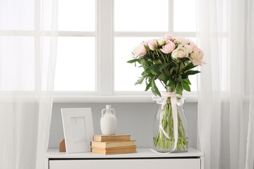 White dresser with books and beautiful peonies in vase near window