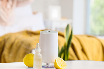 Air humidifier with lemons and essential oil on table against awake woman in bedroom, closeup