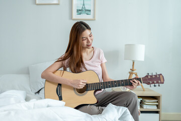 Asian beautiful woman musician playing an acoustic guitar in house.