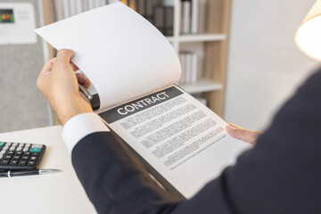 Fototapeta premium A man in a suit is signing a contract. He is holding a pen and looking at the contract 