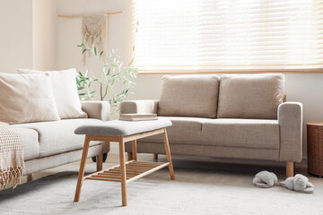 Interior of living room with comfortable beige sofa, bench and books near window