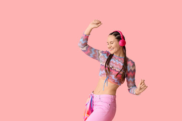 Fashionable young woman in headphones with dreadlocks dancing on pink background