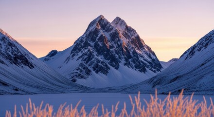 Majestic snowcapped mountain peaks bathed in the soft glow of sunrise or sunset, with a frozen lake in the foreground and frosted reeds