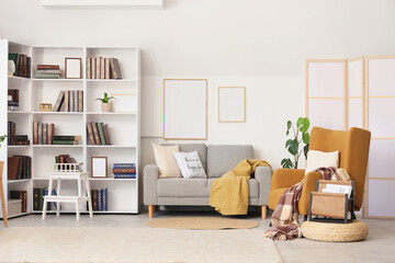 Fototapeta premium Interior of stylish living room with brown armchair, grey sofa and bookshelf