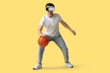 Sporty young man in VR glasses with ball on yellow background