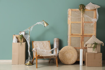 Wrapped furniture with stretch film and boxes near green wall in room on moving day