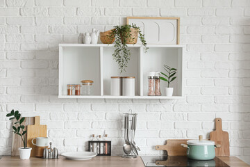 Counter and shelf with utensils on white brick wall in kitchen