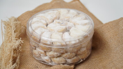 Homemade Putri Salju cookies coated in powdered sugar, stored in a transparent jar. Shot on a clean white background, perfect for festive food promotions and design assets