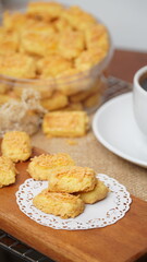 A close-up photo of traditional Indonesian cheese cookies (kastengel) served on a wooden board with a decorative lace paper doily