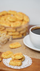 A close-up photo of traditional Indonesian cheese cookies (kastengel) served on a wooden board with a decorative lace paper doily