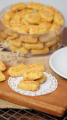 A close-up photo of traditional Indonesian cheese cookies (kastengel) served on a wooden board with a decorative lace paper doily