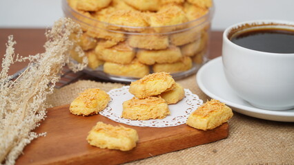 A close-up photo of traditional Indonesian cheese cookies (kastengel) served on a wooden board with a decorative lace paper doily