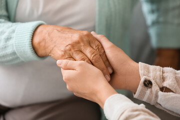 Senior woman with daughter holding hands at home, closeup
