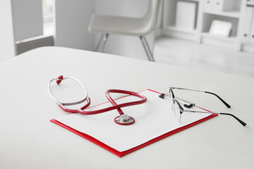 Stethoscope with eyeglasses and clipboard on couch in gynecologist's office, closeup