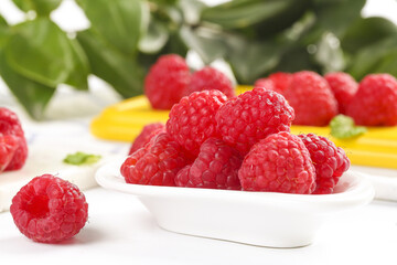 Fresh Red Raspberries in White Bowl with Flowers and Green Leaves Background