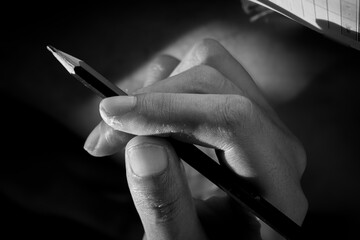 Close-up of a hand holding a pencil in dramatic lighting, black and white photography emphasizing texture, detail, and contrast © FeriFerdinan
