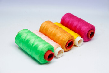 A vibrant, 45-degree shot of five spools of thread. The colorful spools light green, light pink, orange, yellow, and bright red showcase a beautiful palette. Perfect for craft, sewing, and hobby theme