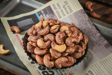 Salt-Baked Cashew Nuts with Purple Crispy Shells in Metal Bowl on Newspaper Background
