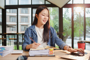 Smiling young Asian woman clearing paperwork in office, using laptop and many documents beside her. Accounting and finance business concept.