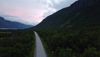 Scenic mountain road winding through lush green forest under a dramatic cloudy sky.